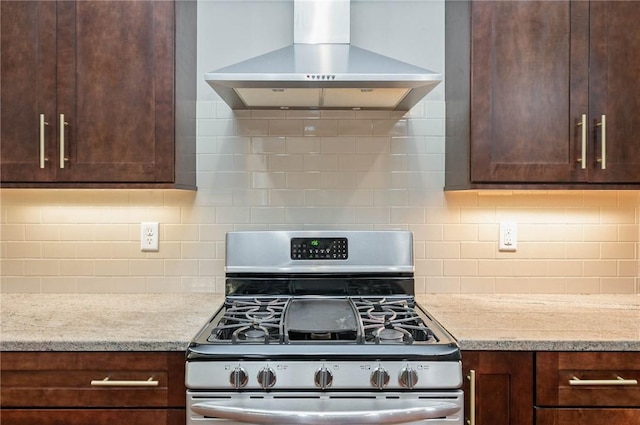 kitchen featuring decorative backsplash, light stone countertops, wall chimney range hood, and stainless steel range with gas stovetop