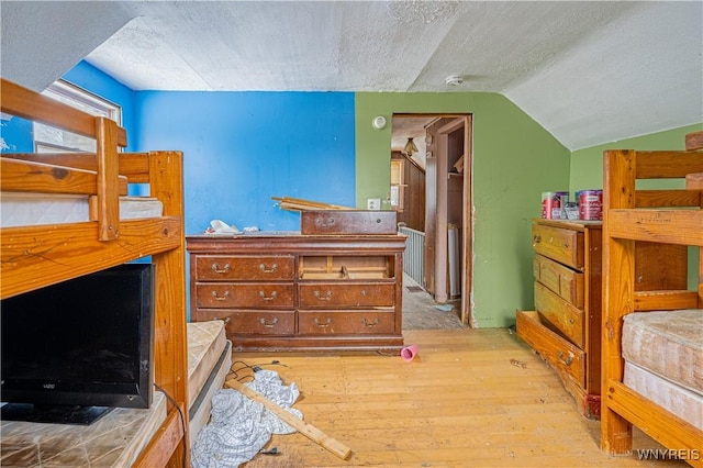 bedroom featuring lofted ceiling, light hardwood / wood-style floors, and a textured ceiling