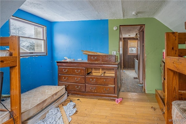 bedroom with lofted ceiling, a textured ceiling, and light wood-type flooring