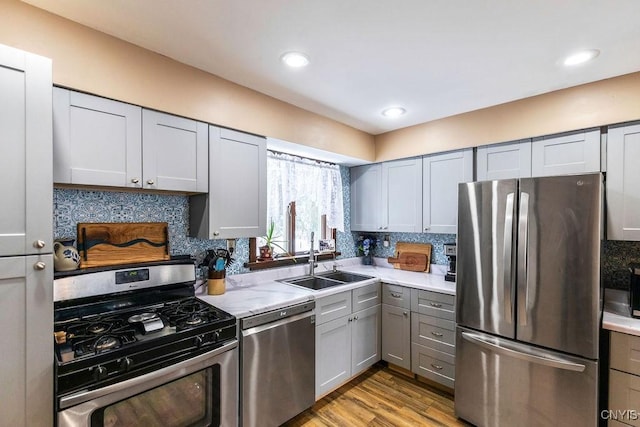 kitchen with appliances with stainless steel finishes, light wood-type flooring, backsplash, gray cabinetry, and sink