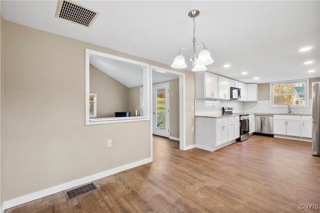 kitchen featuring white cabinetry, sink, hanging light fixtures, decorative backsplash, and appliances with stainless steel finishes