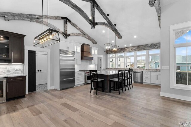 kitchen featuring premium appliances, dark brown cabinets, decorative light fixtures, and custom exhaust hood