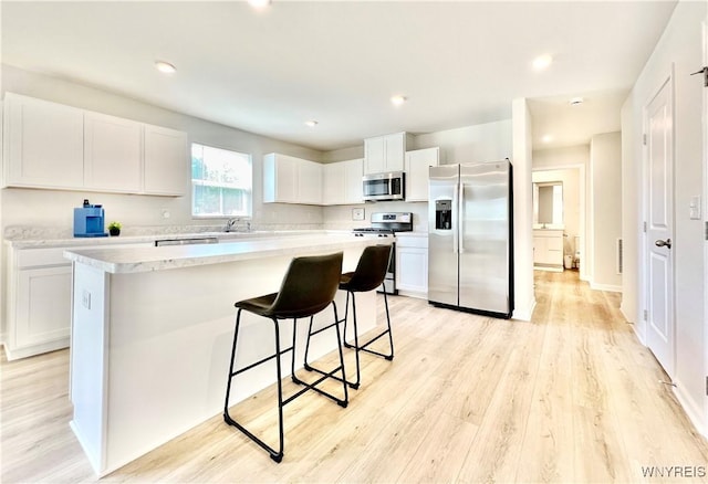 kitchen with white cabinets, light hardwood / wood-style flooring, a breakfast bar area, a kitchen island, and appliances with stainless steel finishes