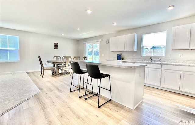 kitchen with white cabinets, a center island, light stone counters, and light hardwood / wood-style flooring