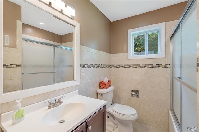 full bathroom with vanity, bath / shower combo with glass door, tile walls, and toilet