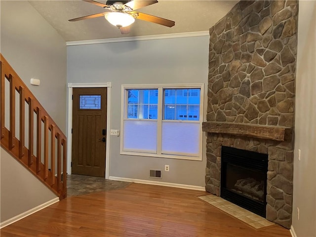 foyer featuring hardwood / wood-style floors, a stone fireplace, ceiling fan, and ornamental molding