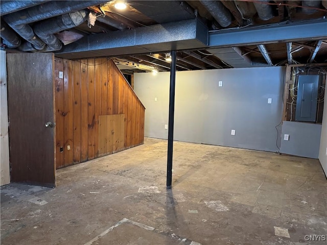 basement with electric panel and wooden walls