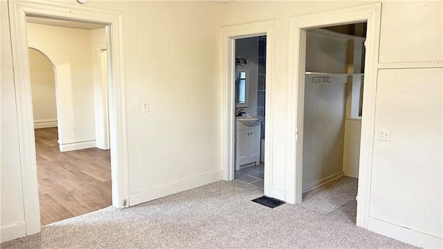 unfurnished bedroom featuring connected bathroom, a closet, sink, and light colored carpet