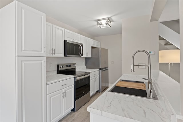 kitchen featuring white cabinetry, sink, light stone countertops, decorative backsplash, and appliances with stainless steel finishes