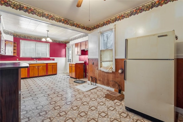 kitchen with ceiling fan with notable chandelier, sink, wooden walls, decorative light fixtures, and white fridge