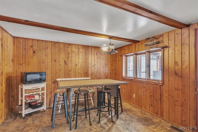 dining area with wooden walls, beamed ceiling, and a notable chandelier