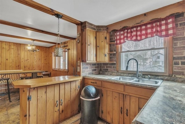 kitchen featuring pendant lighting, beam ceiling, sink, and wooden walls