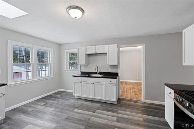 kitchen with sink, a skylight, white cabinetry, dark hardwood / wood-style flooring, and range