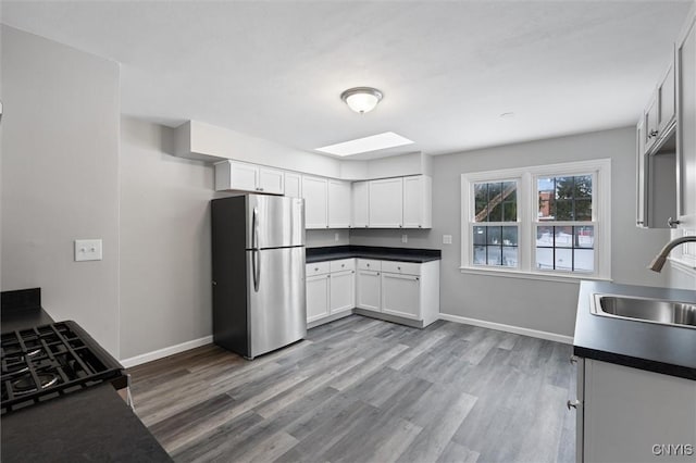 kitchen with sink, a skylight, light wood-type flooring, white cabinetry, and stainless steel refrigerator