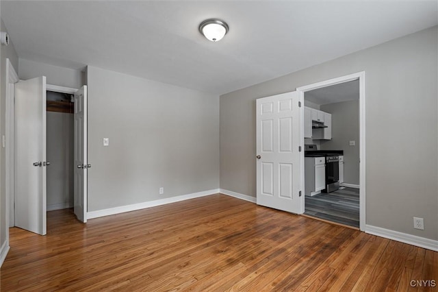 unfurnished bedroom with ensuite bathroom, a closet, and wood-type flooring