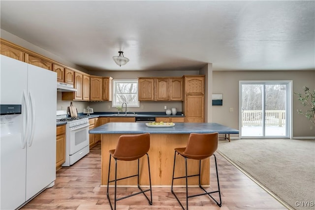 kitchen with a center island, sink, light colored carpet, white appliances, and a breakfast bar