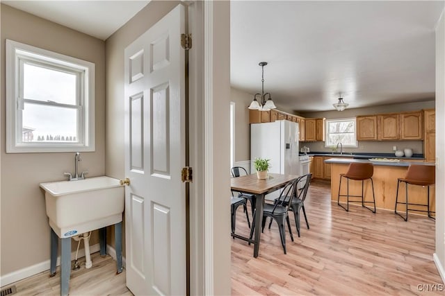 kitchen with a kitchen breakfast bar, decorative light fixtures, an inviting chandelier, light hardwood / wood-style flooring, and white fridge with ice dispenser