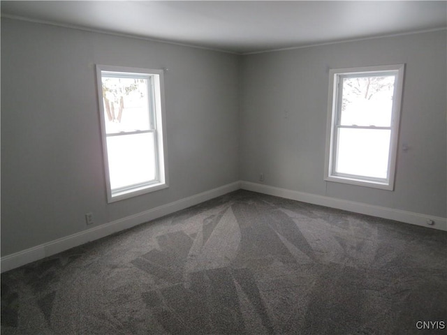 unfurnished room featuring dark colored carpet, crown molding, and a wealth of natural light