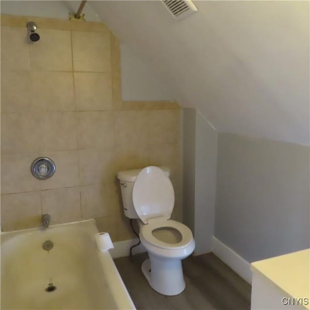 bathroom with wood-type flooring, tile walls, toilet, tiled shower / bath, and lofted ceiling