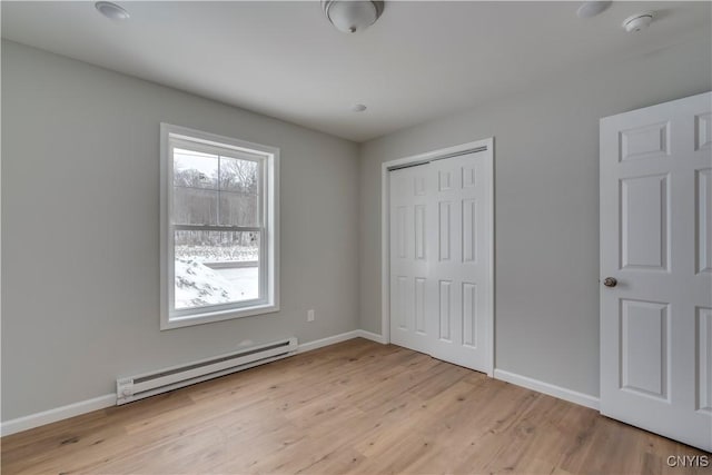 unfurnished bedroom featuring baseboard heating, a closet, and light hardwood / wood-style flooring