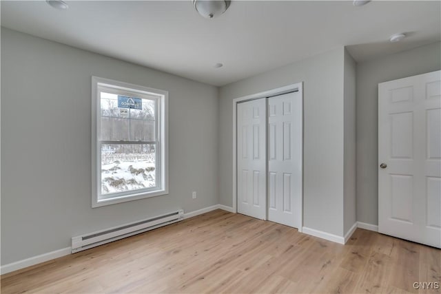 unfurnished bedroom with light wood-type flooring, baseboard heating, and a closet