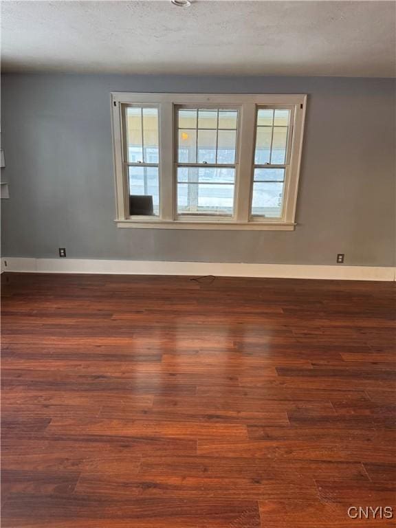 spare room with a textured ceiling, plenty of natural light, and dark wood-type flooring