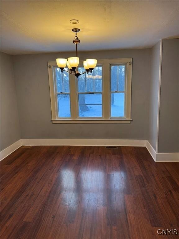 unfurnished dining area with dark wood-type flooring and an inviting chandelier