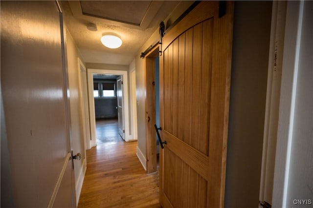 hall with a barn door, light wood-type flooring, and a textured ceiling