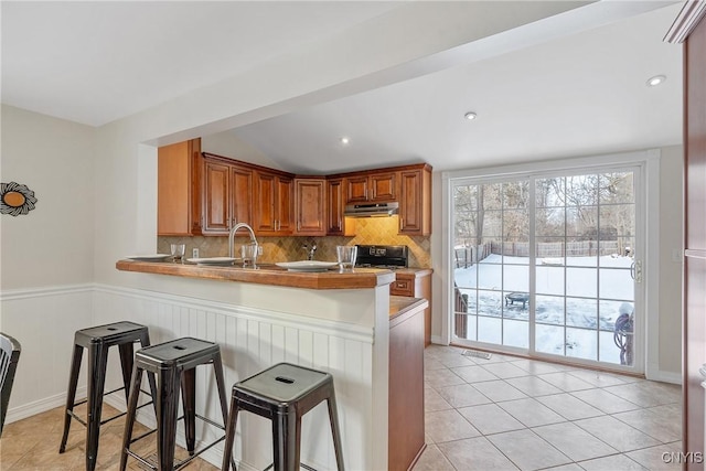 kitchen with a kitchen breakfast bar, decorative backsplash, kitchen peninsula, and light tile patterned floors