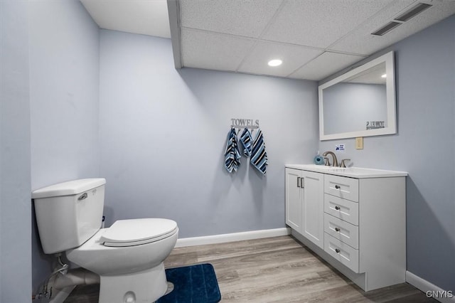 bathroom with a paneled ceiling, hardwood / wood-style flooring, vanity, and toilet