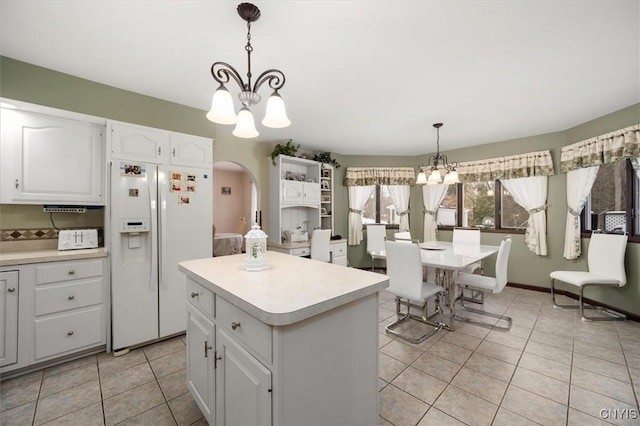 kitchen featuring a kitchen island, white refrigerator with ice dispenser, decorative light fixtures, a notable chandelier, and white cabinetry