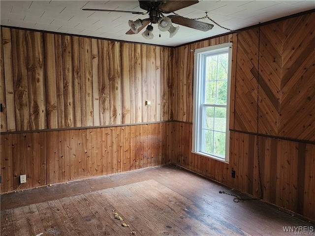 empty room with ceiling fan, wooden walls, and hardwood / wood-style flooring