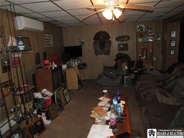 living room with carpet, a paneled ceiling, ceiling fan, wooden walls, and an AC wall unit