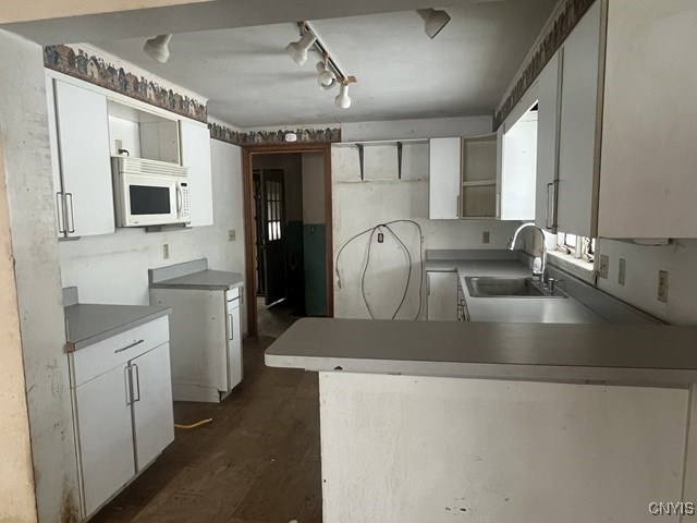 kitchen featuring kitchen peninsula, rail lighting, sink, dark hardwood / wood-style floors, and white cabinetry