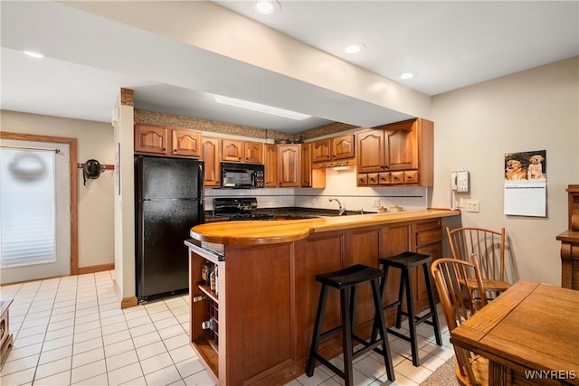 kitchen with sink, a kitchen breakfast bar, kitchen peninsula, light tile patterned floors, and black appliances