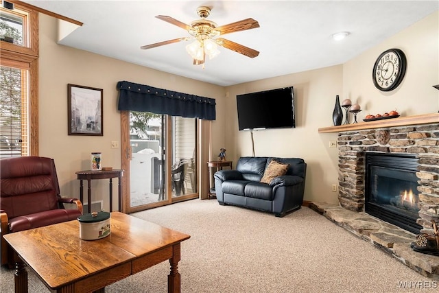 carpeted living room featuring ceiling fan and a stone fireplace