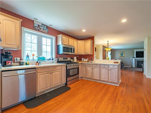 kitchen featuring sink, a brick fireplace, appliances with stainless steel finishes, decorative light fixtures, and kitchen peninsula