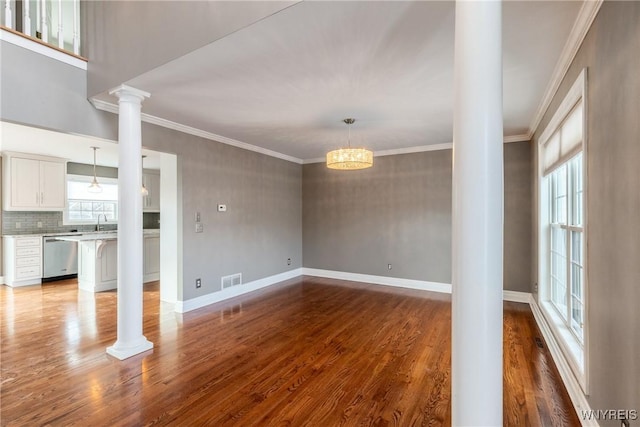 unfurnished living room featuring hardwood / wood-style floors, a chandelier, ornamental molding, and decorative columns