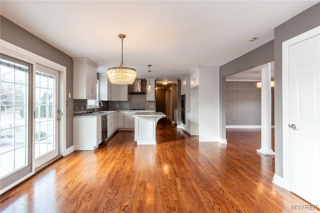 kitchen featuring tasteful backsplash, stainless steel dishwasher, wall chimney range hood, decorative light fixtures, and a kitchen island