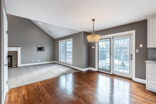 unfurnished dining area with wood-type flooring, vaulted ceiling, a notable chandelier, and a stone fireplace