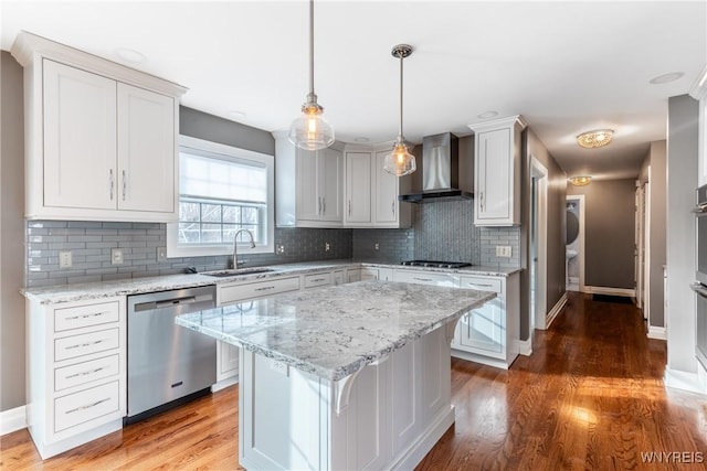 kitchen with sink, wall chimney exhaust hood, appliances with stainless steel finishes, a kitchen island, and white cabinetry