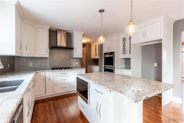 kitchen featuring a center island, wall chimney exhaust hood, hanging light fixtures, stainless steel appliances, and decorative backsplash