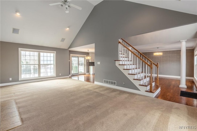 unfurnished living room with dark colored carpet, ceiling fan with notable chandelier, high vaulted ceiling, and decorative columns