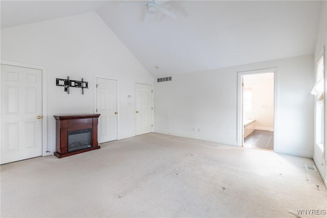 unfurnished living room with ceiling fan, a healthy amount of sunlight, light colored carpet, and high vaulted ceiling