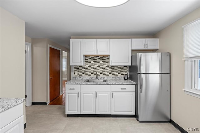 kitchen featuring light stone countertops, white cabinetry, sink, and stainless steel refrigerator