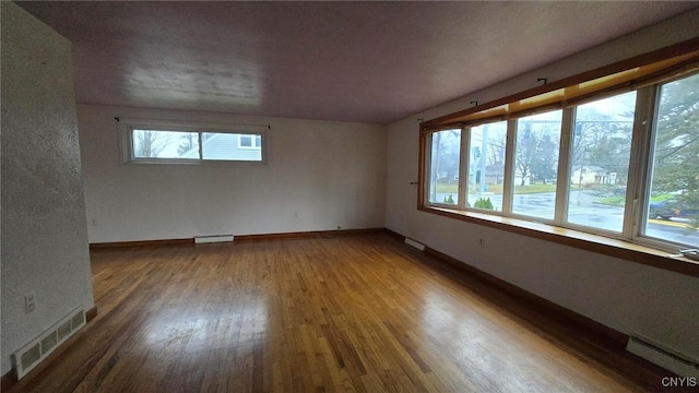 empty room with a healthy amount of sunlight, hardwood / wood-style flooring, and a baseboard heating unit