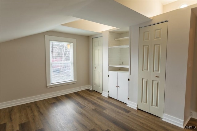 unfurnished bedroom featuring vaulted ceiling, dark wood-type flooring, and two closets