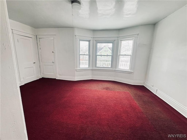 spare room with baseboards and dark colored carpet