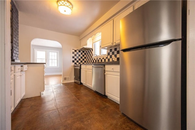 kitchen with dark tile patterned floors, white cabinetry, backsplash, and appliances with stainless steel finishes