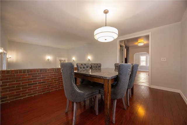 dining space with dark wood-type flooring and brick wall